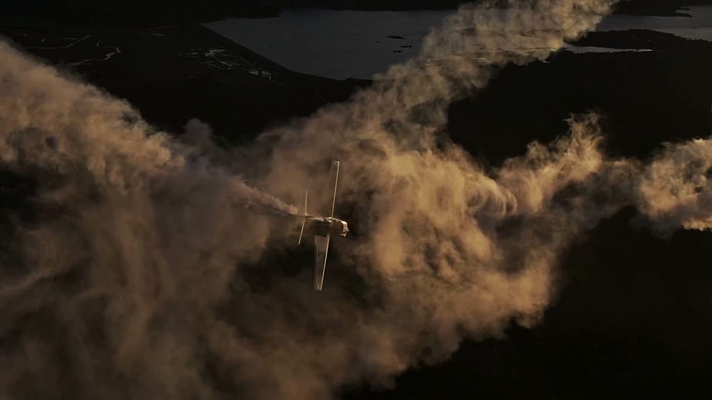 Aerobatic aircraft trailing smoke over mountains, filmed air-to-air