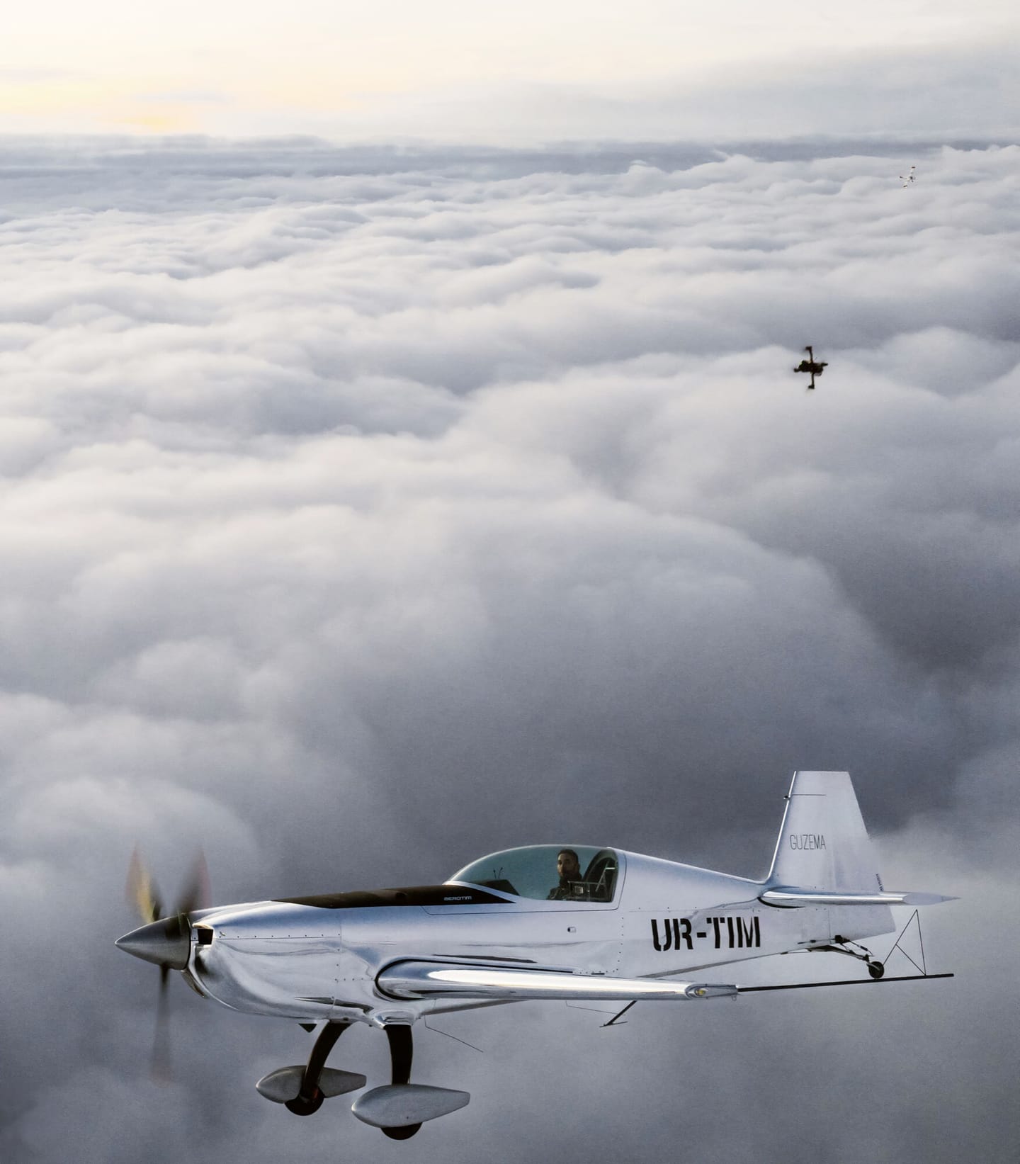 Silver aerobatic aircraft above the clouds with an FPV camera aircraft