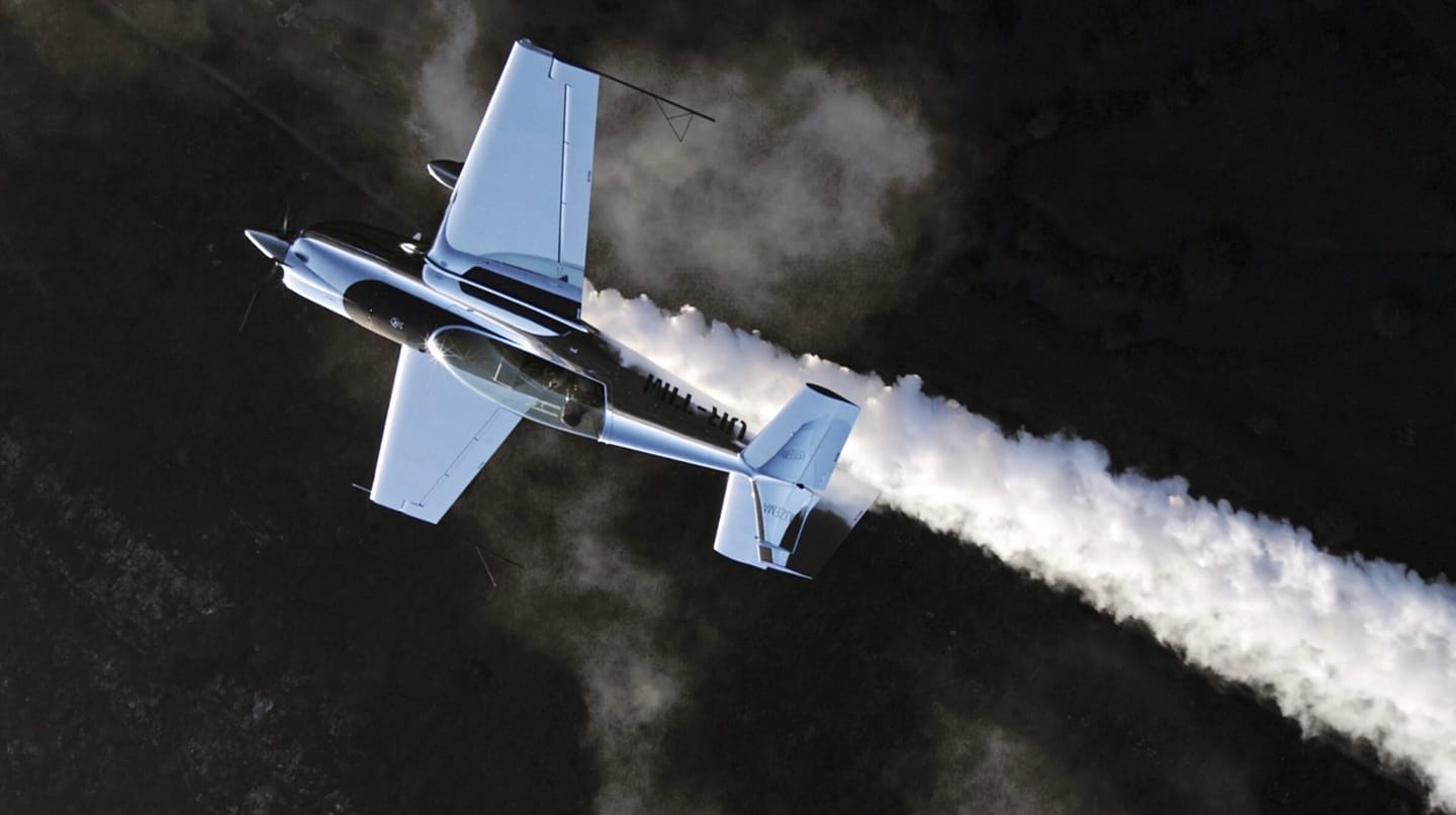 Aerobatic aircraft with smoke trail, top-down from the camera ship